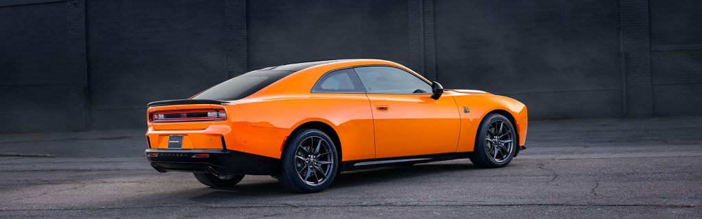 Orange Dodge Charger parked in front of a dark brick wall.