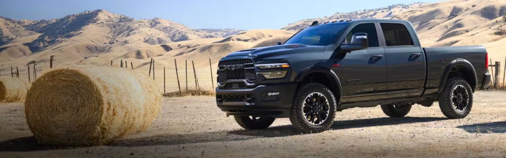 Black RAM 2500 Rebel parked in a field with hay bales and rolling hills.
