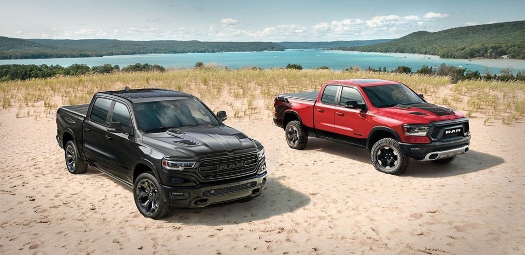 A black Ram 1500 and a red Ram 1500 Rebel parked on a sandy beach.