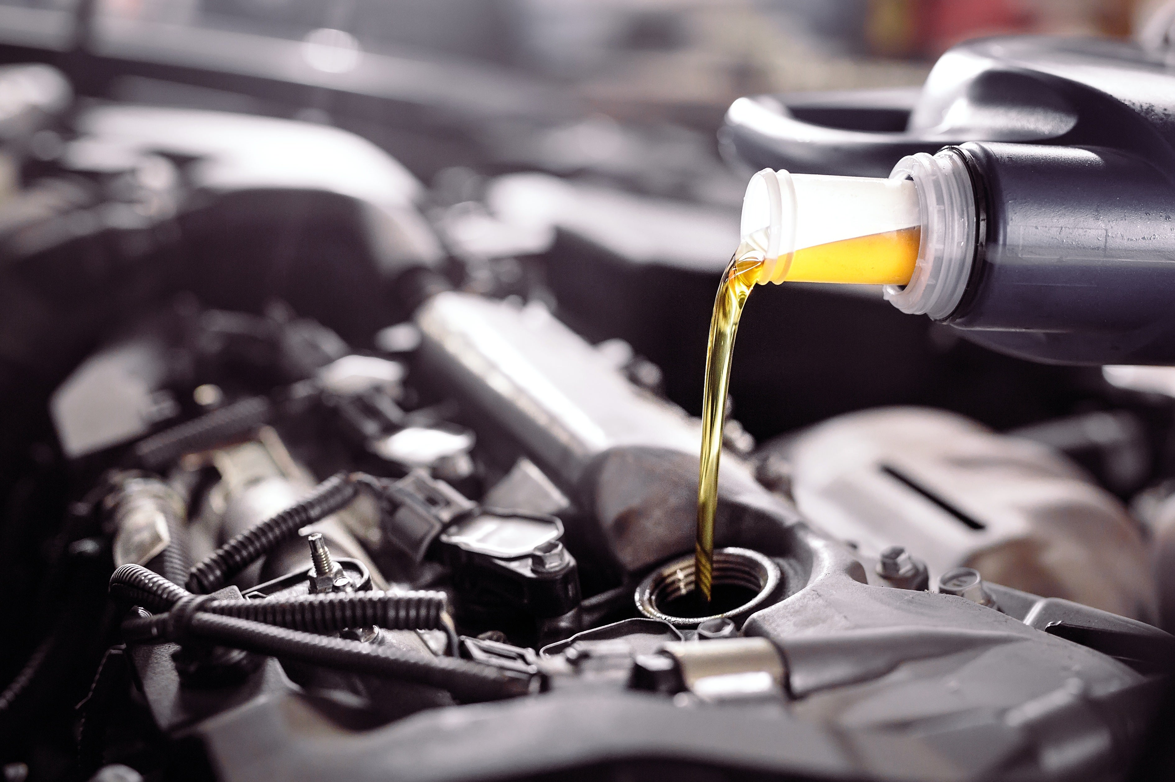 Golden motor oil being poured from a bottle into a car engine’s oil filler opening.